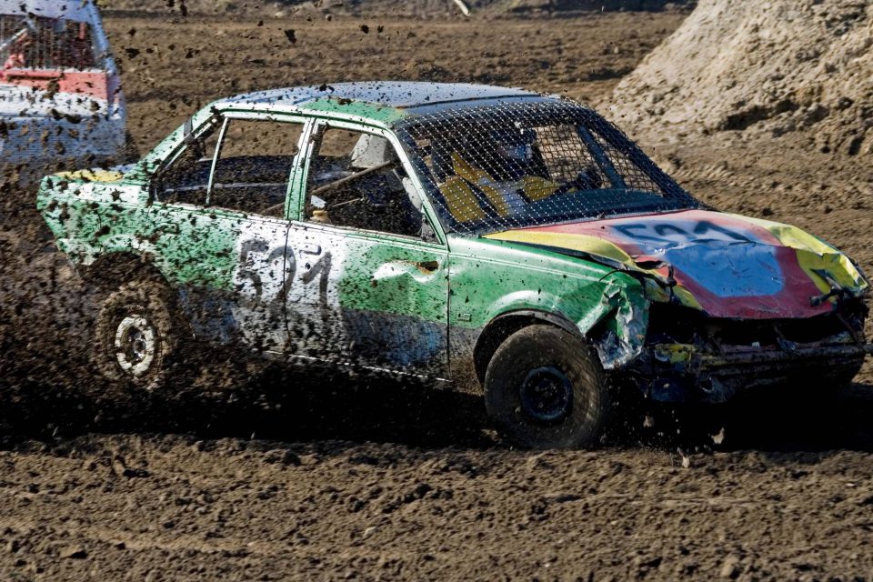 Multicolored demolition derby car driving through mud.