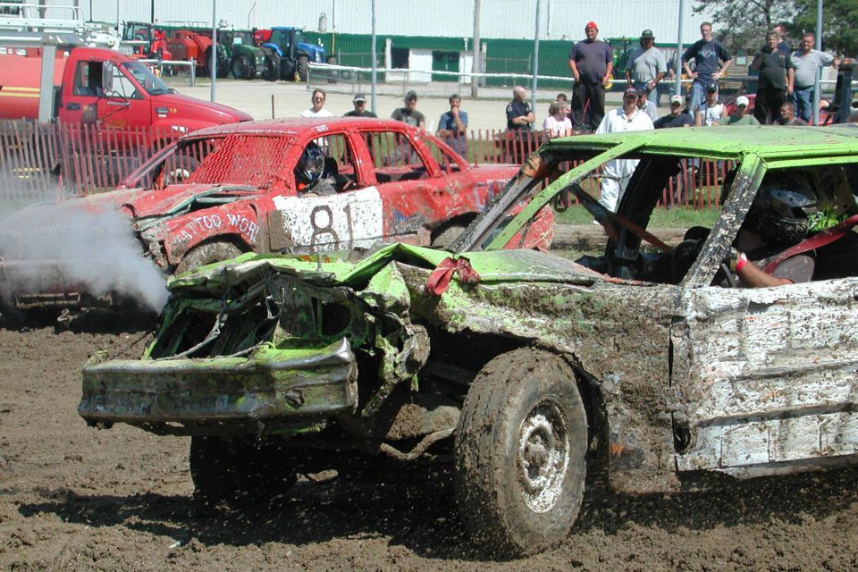 Demolition derby competition cars with audience looking on.